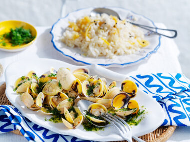 Lemon rice with vongole and dill oil on white dish with blue and white patterned napkin and silver knife and fork.