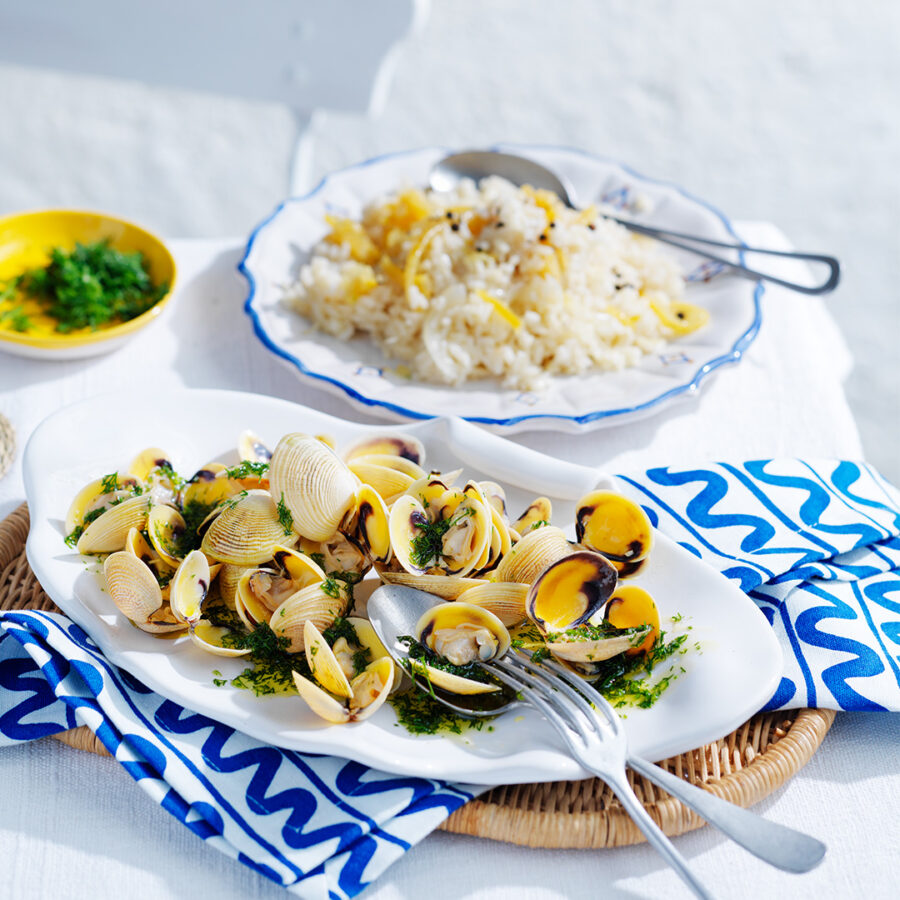 Lemon rice with vongole and dill oil on white dish with blue and white patterned napkin and silver knife and fork.