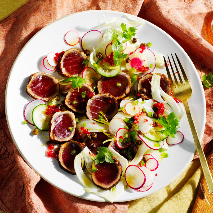 Spiced tuna, radishes, micro greens and finger lime with a gold fork on a white plate.