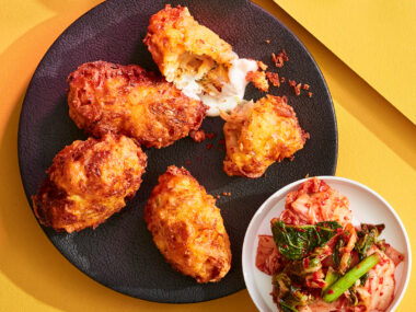 Korean kimchi fritters on black plate with bowl of kimchi to side on yellow background.