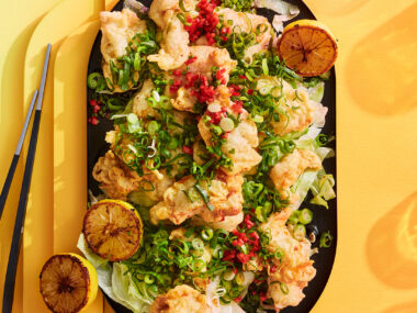 Lemon soy chicken with lemon wedges on a black platter, yellow background.