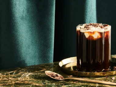 An Irish Coffee cocktail served in a clear ridged glass with an emerald green background