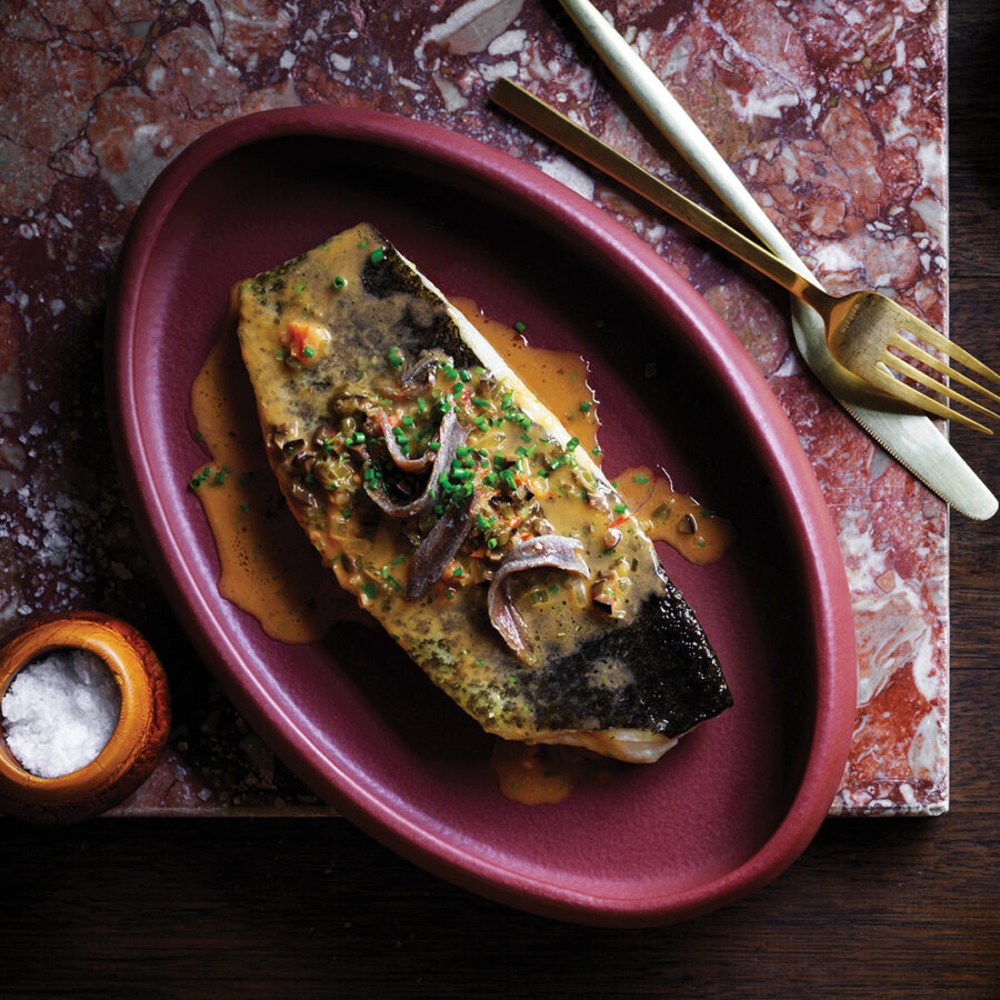 Roast murray cod with puttanesca butter topped with anchovies in purple bowl.