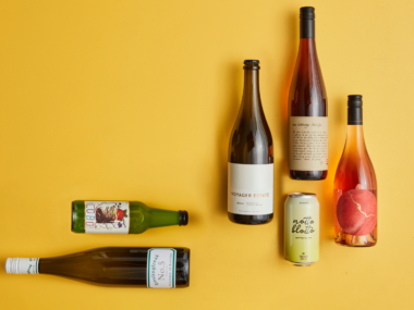 Five wine bottles and one can laid out against an orange background