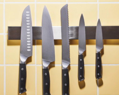 Kitchen knives hanging in a row against a yellow-tiled background